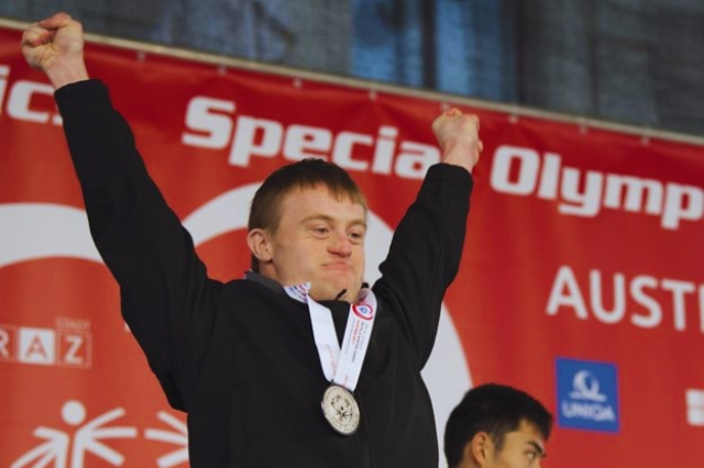 Man with disability holding his hands up in victory at the Special Olympics with a medal around his neck.