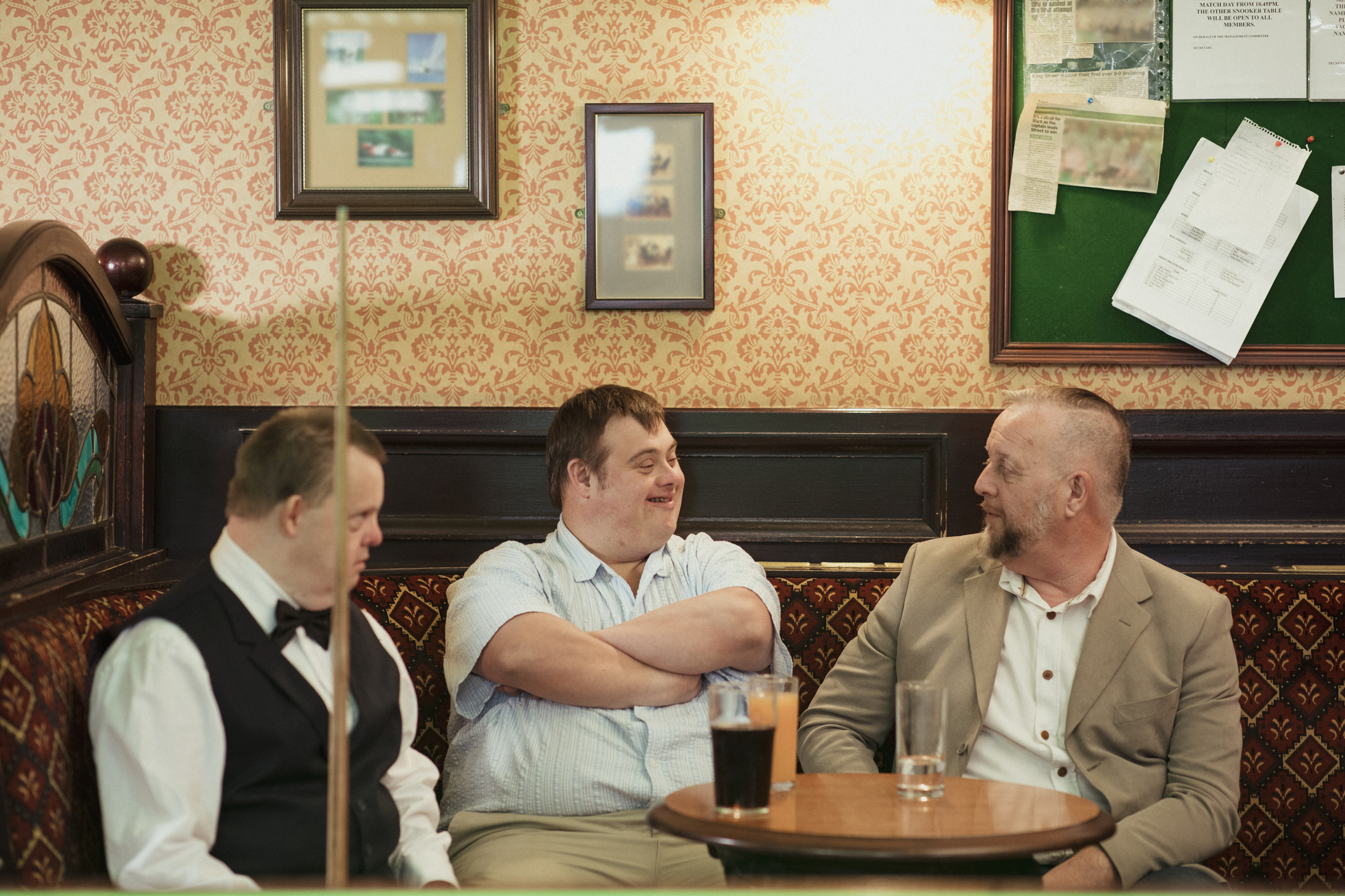 Two men with disabilities in a bar having a casual conversation with a non-disabled male buddy