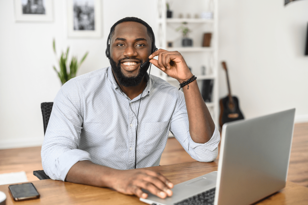 Remote Support Staff who is a male.  Sitting at a desk with laptop and headphones smiling