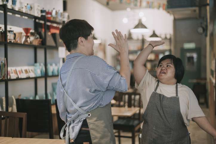 asian cafe down syndrome disability employee high five dancing with owner bonding time in cafe happily two hands holding with the words skills, knowledge, growth, training, experience