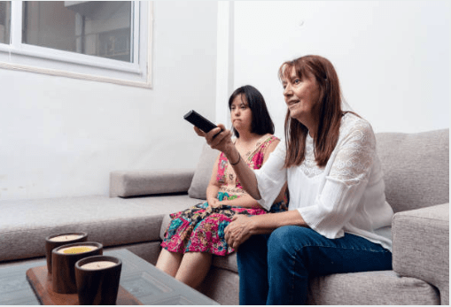 Down syndrome girl with family playing games Caregiver and young woman with down syndrome sitting on the couch. Caregiver has remote in her hand