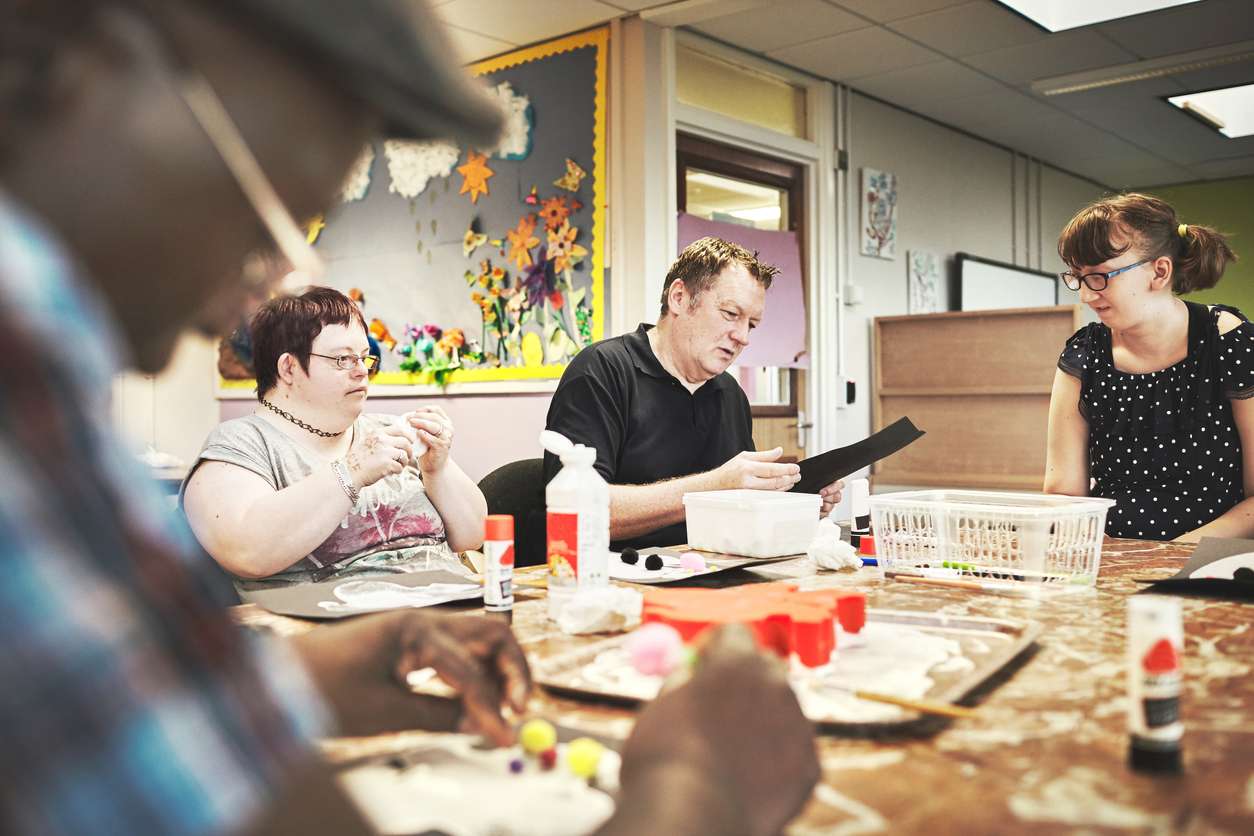 Disability health care art workshop, creative paint and down syndrome people doing a project. Disabled painter group relax working with craft tools to do a special needs painting with a brush Group of people with disabilities meeting and talking around a table