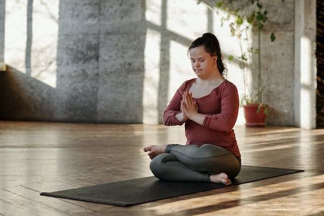 Young Woman with down syndrome is sitting on a mat, mediating.