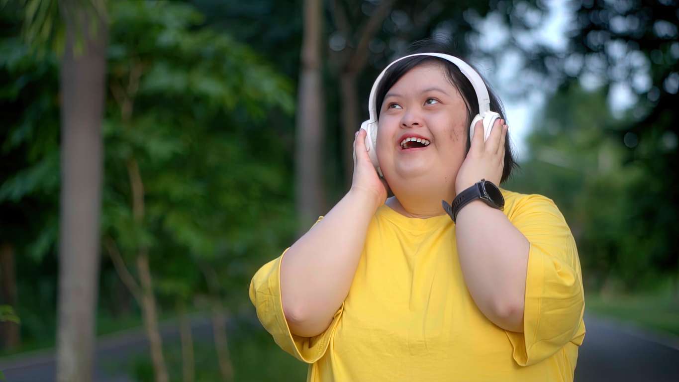 Down syndrome girl exercising in the park wearing headphones. Girl with Autism in Yellow shirt and white headphones