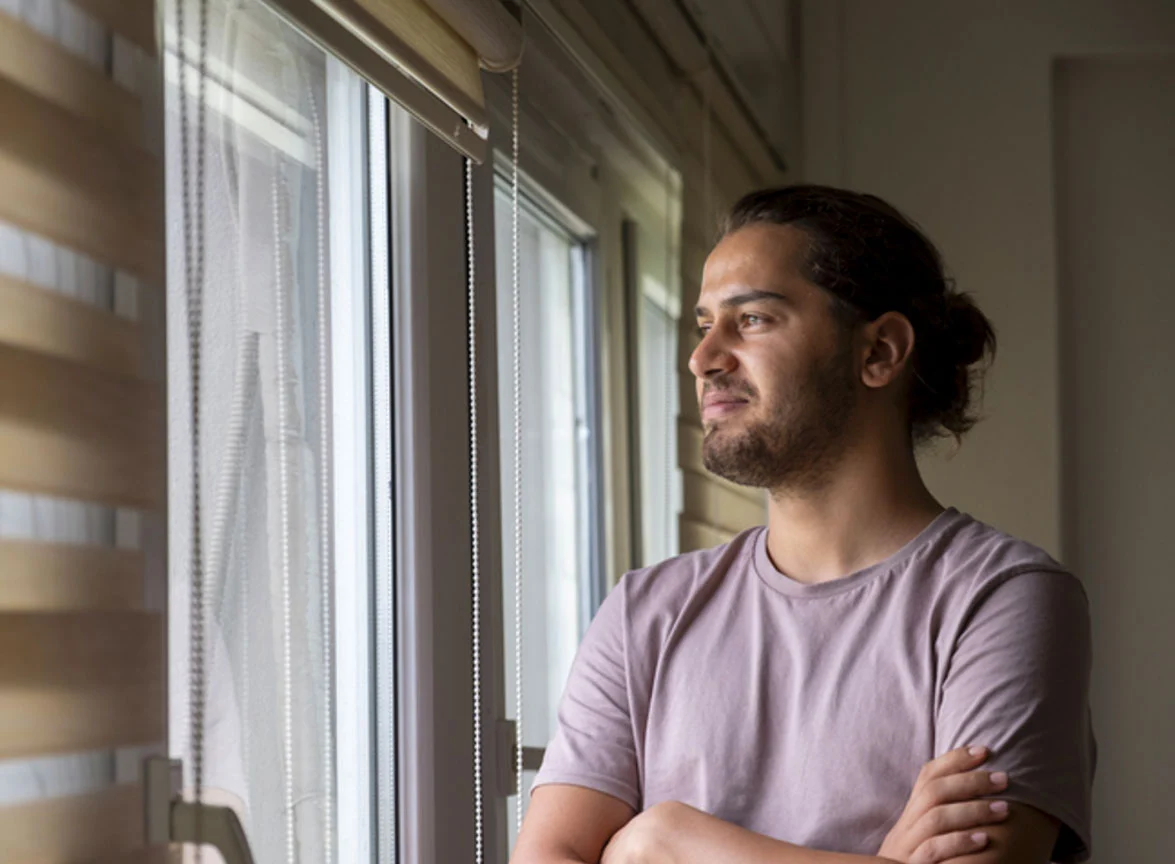 Man with crossed arms looking out window.